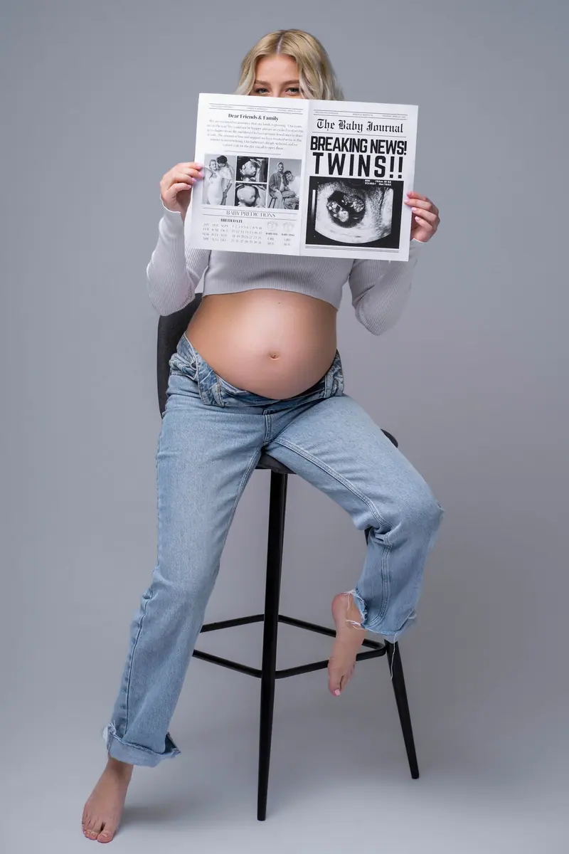 Tehotenské fotenie — tehotná na stoličke drží noviny „TWINS“