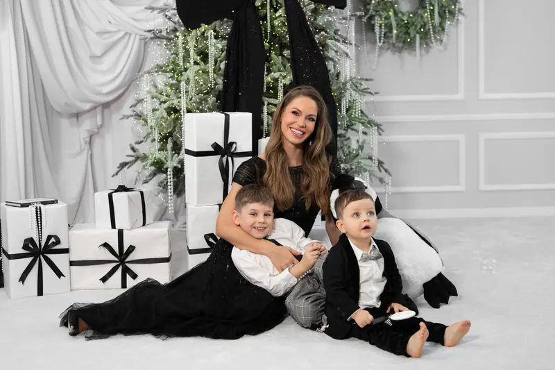 Vianočné fotenie — mama leží s dvoma chlapcami pri darčekoch, čierno-biela scéna