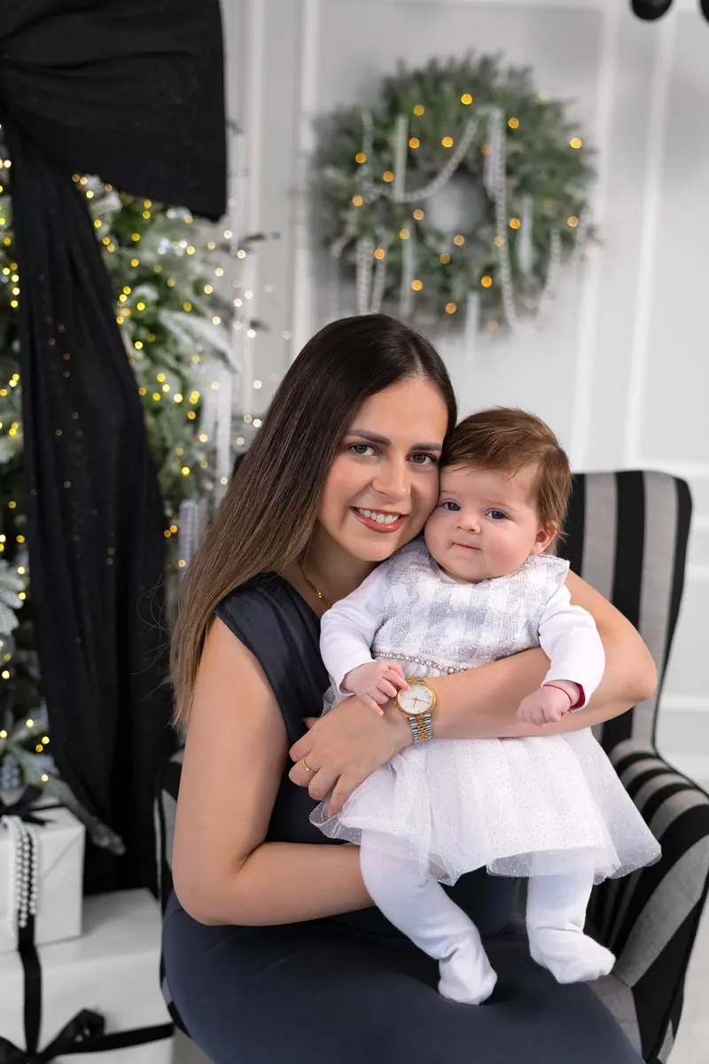 Vianočné fotenie — mama drží bábätko v bielych šatôčkach, pruhované kreslo