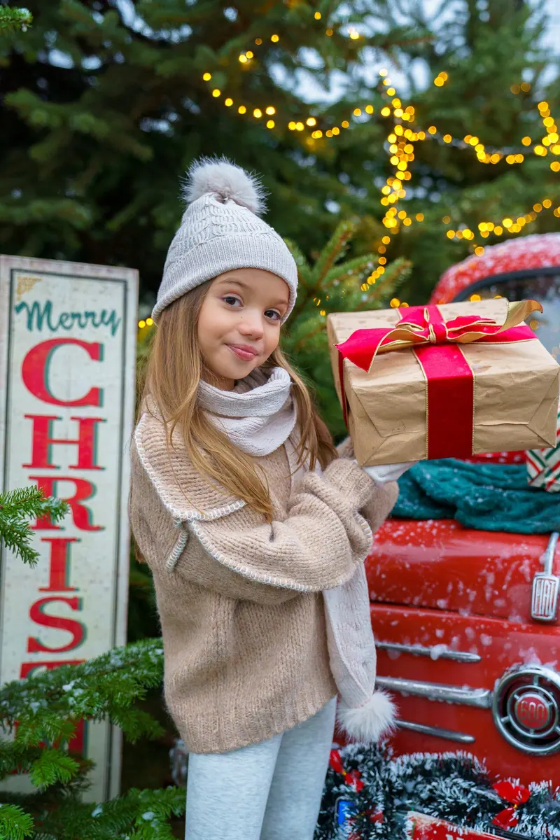 Fotenie v exteriéri — dievčatko drží darček pri tabuli „Merry Christmas“